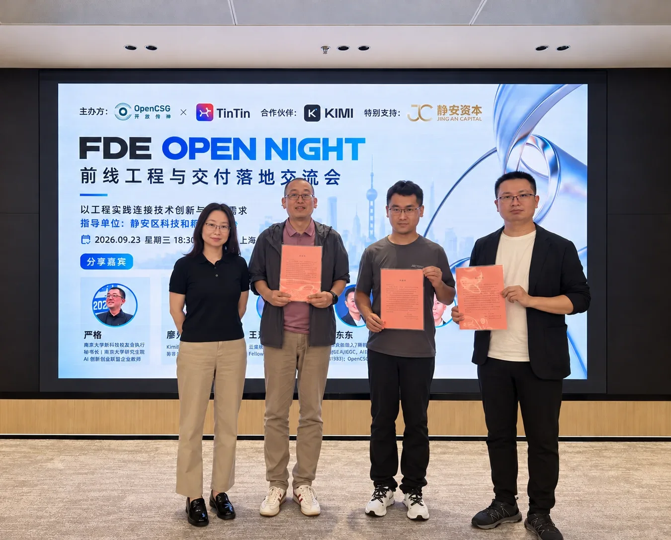 Participants holding event recognition letters in front of the FDE Open Night screen